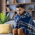 Man,Wrapped,In,Checkered,Blanket,Sitting,On,Sofa,,Looks,Cold
